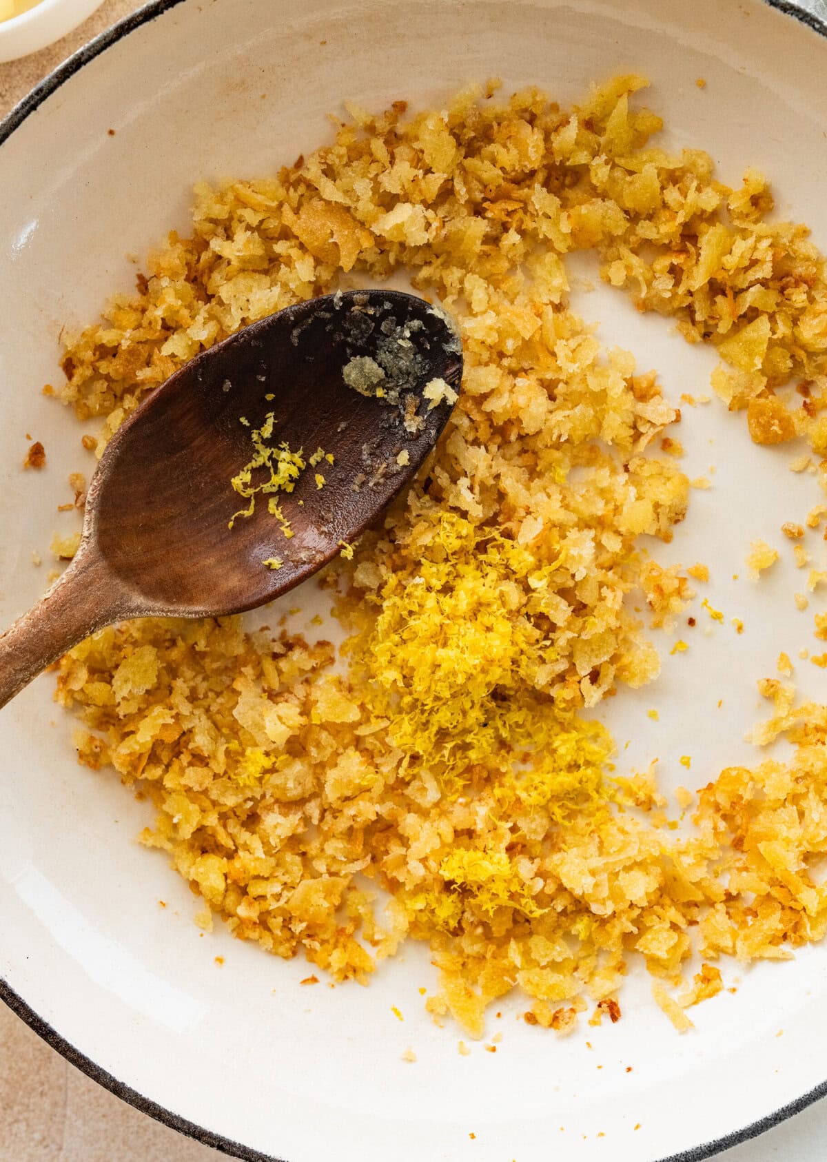 Spoon resting in a skillet after combining the breadcrumb topping.