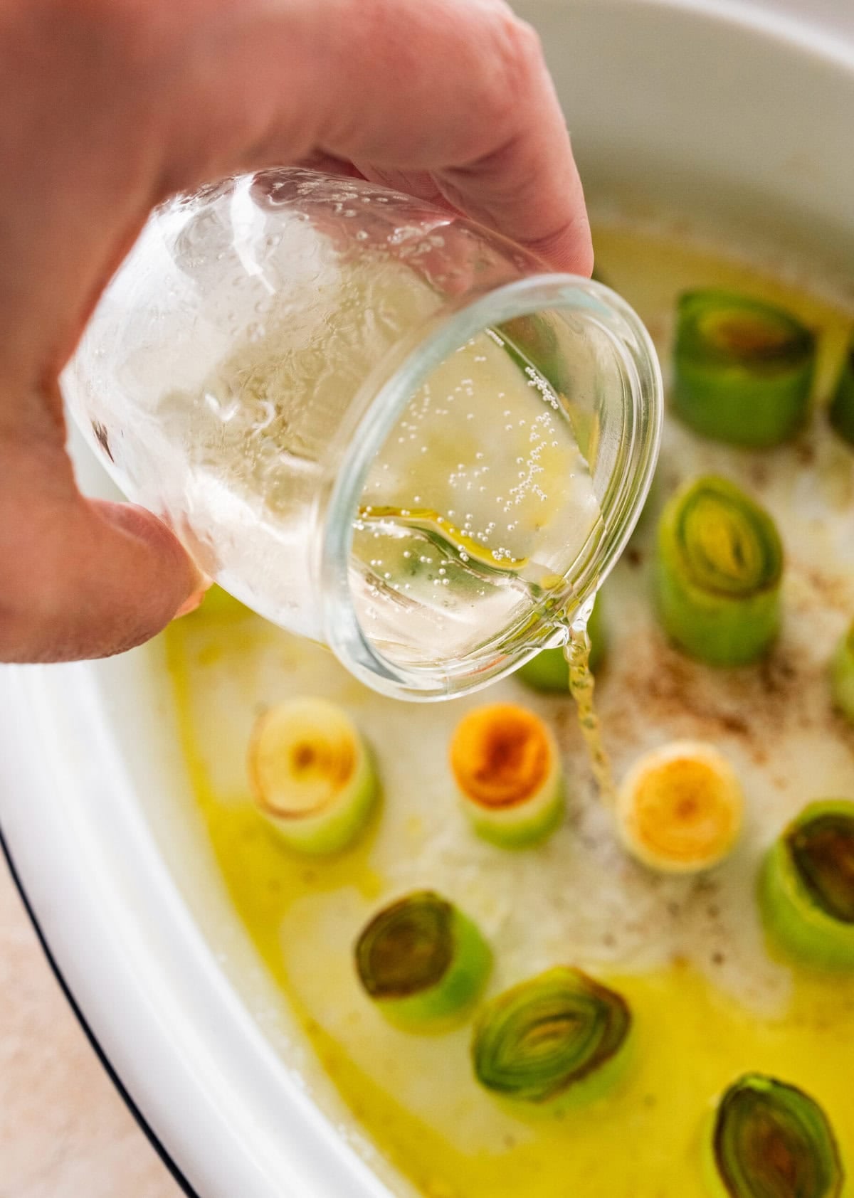 White wine being poured into the skillet over the leeks.