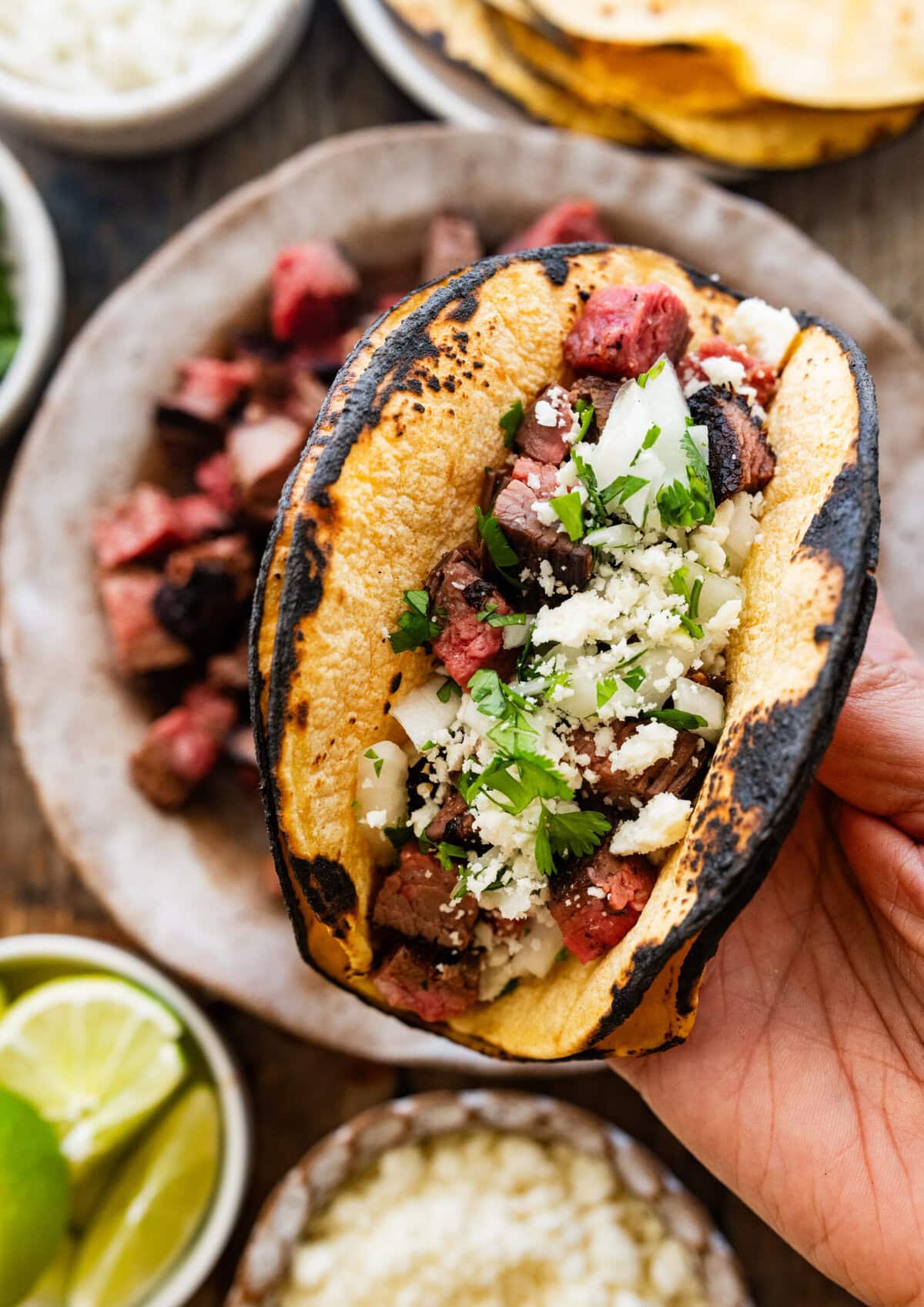 One taco filled with toppings, held over more toppings.