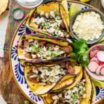 Multiple tacos filled with tacos presented on a plate, with more taco toppings on the side.