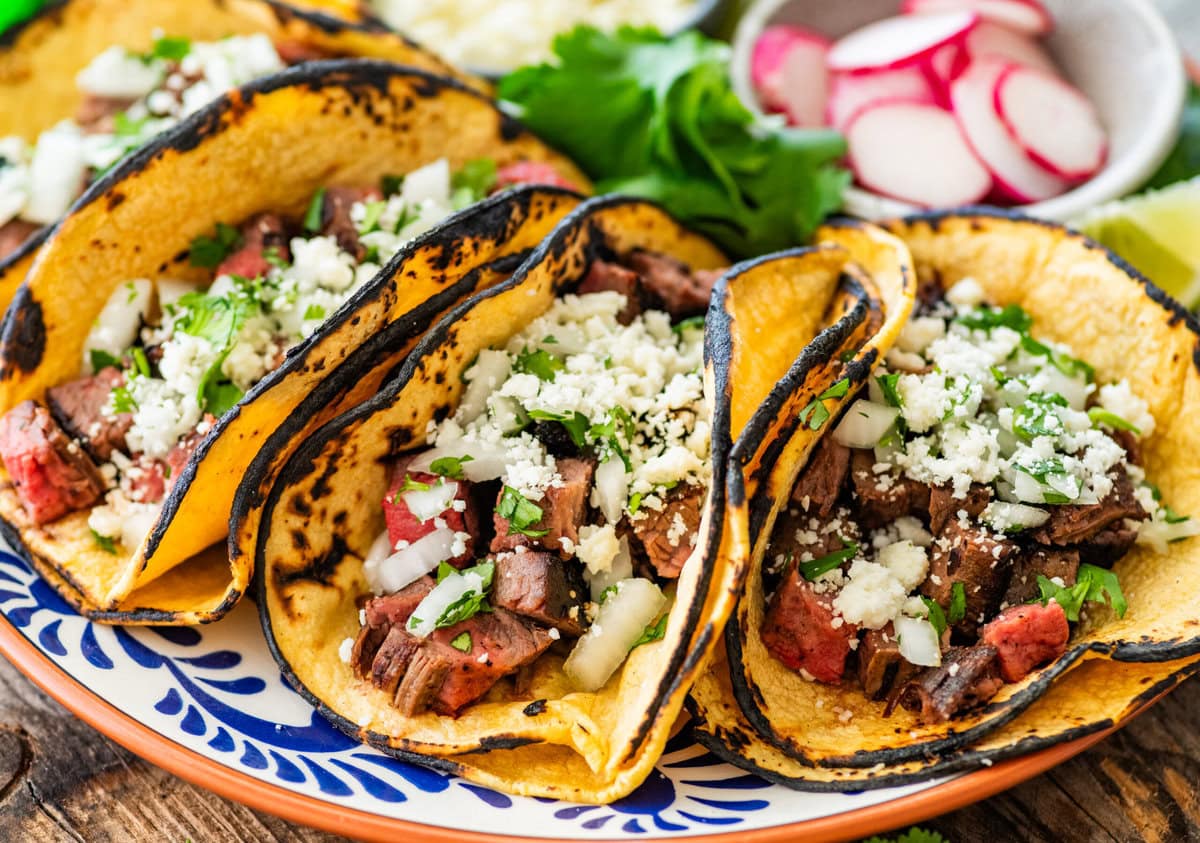 Multiple tacos filled with tacos presented on a plate, with more taco toppings on the side.
