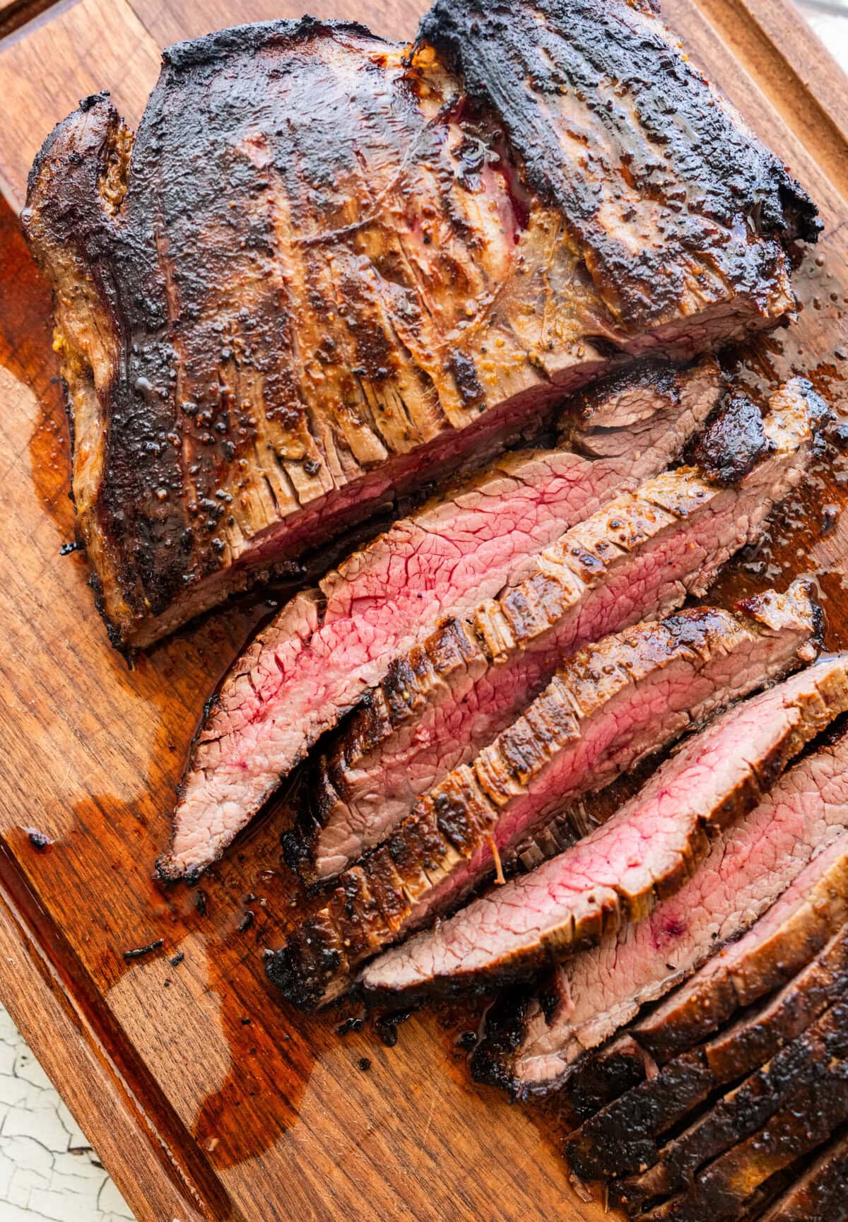 Steak on a cutting board, with half of it cut into slices.