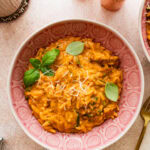 Chicken and orzo in a bowl garnished with basil, with other bowl of chicken and orzo in the background.