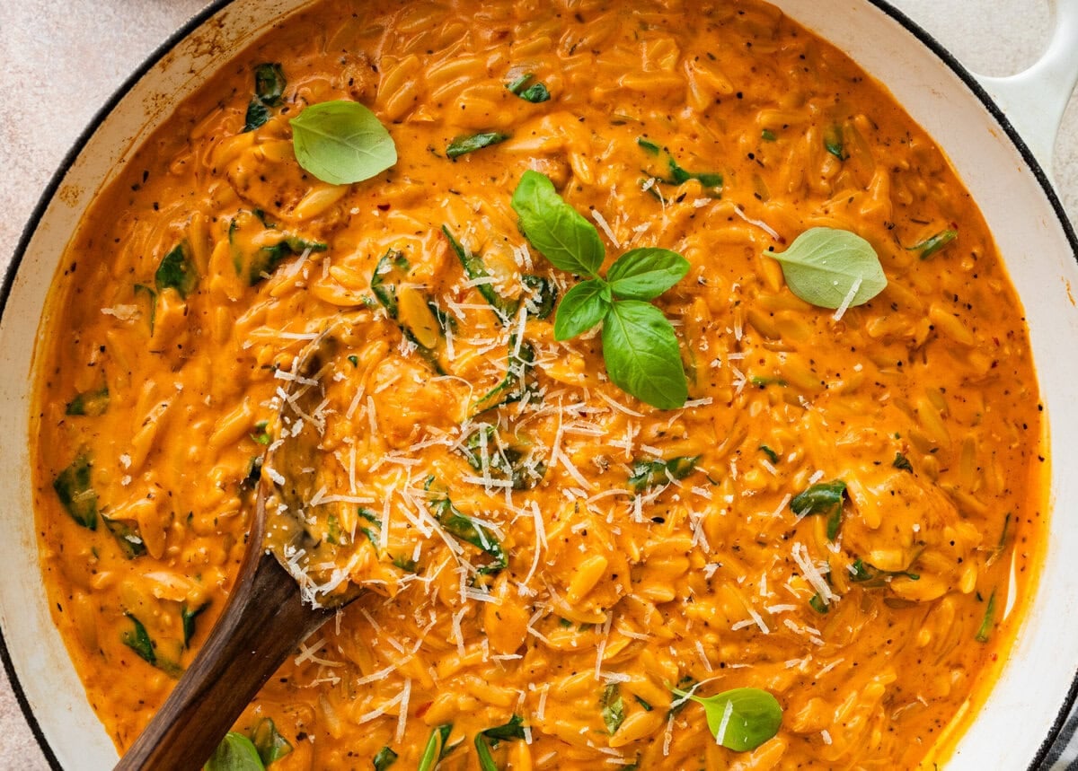 Pot of creamy chicken orzo garnished with basil, with a spoon resting in the pot.