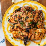 Chicken on a serving dish with garnish, and more sides surrounding.