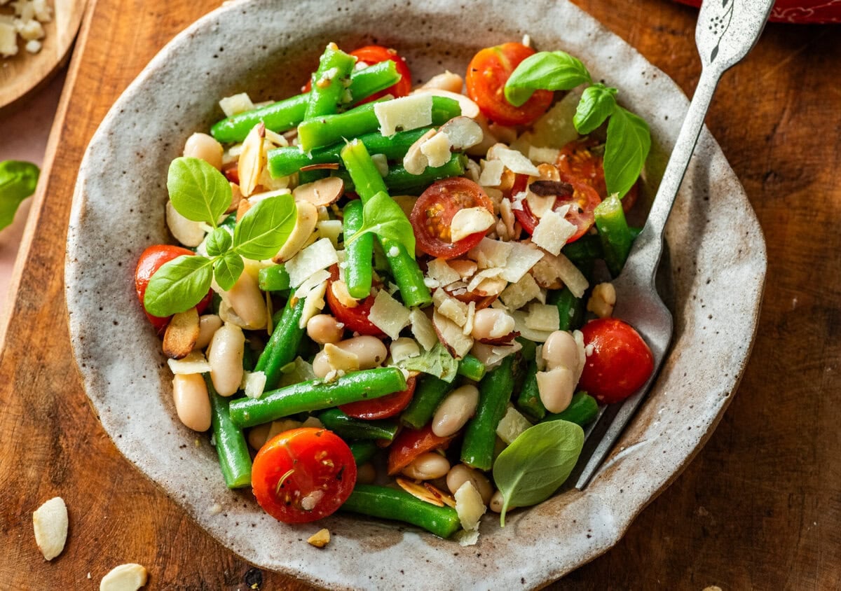 Green bean salad in a serving bowl with serving utensil resting in it.