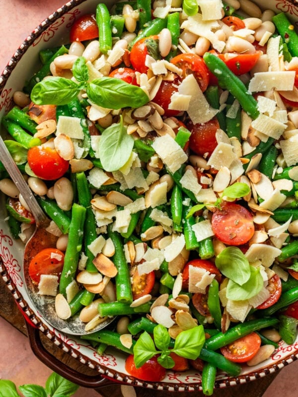 Green bean salad in a serving bowl with serving utensil resting in it.
