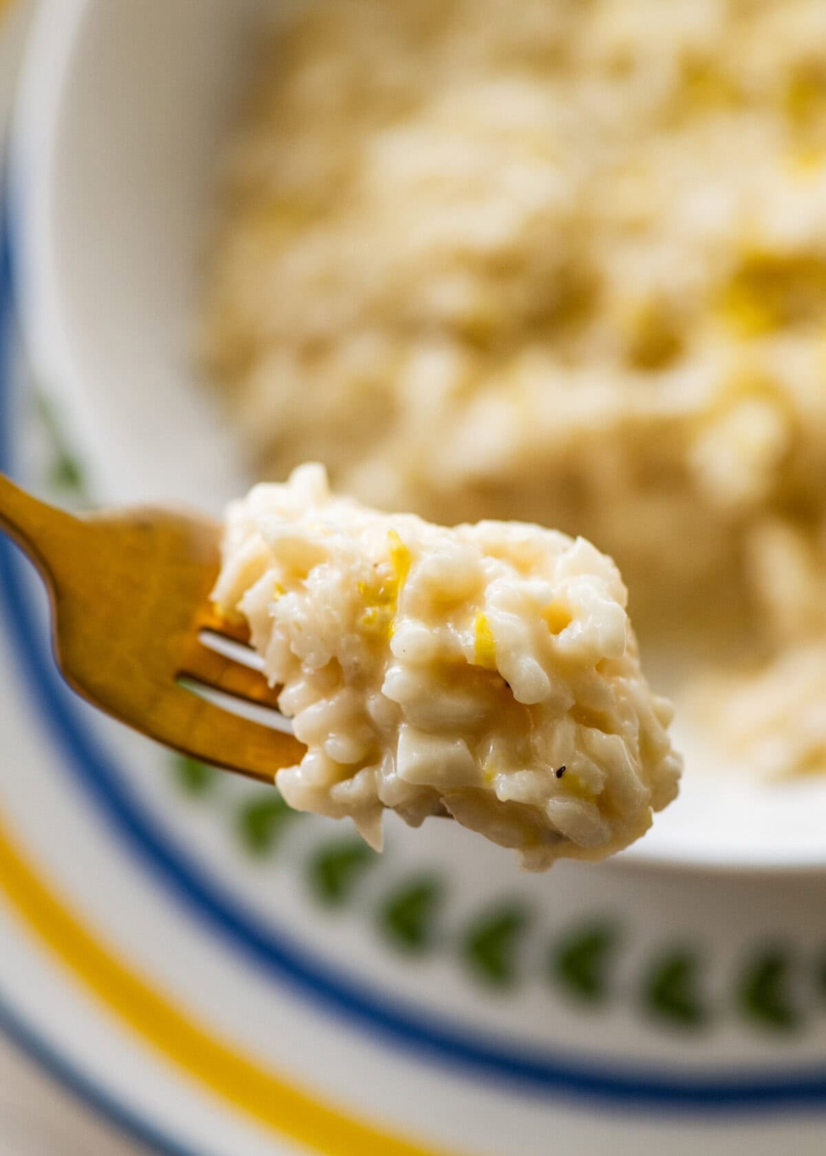 One bite of lemon risotto on a fork held over a bowl of more risotto.