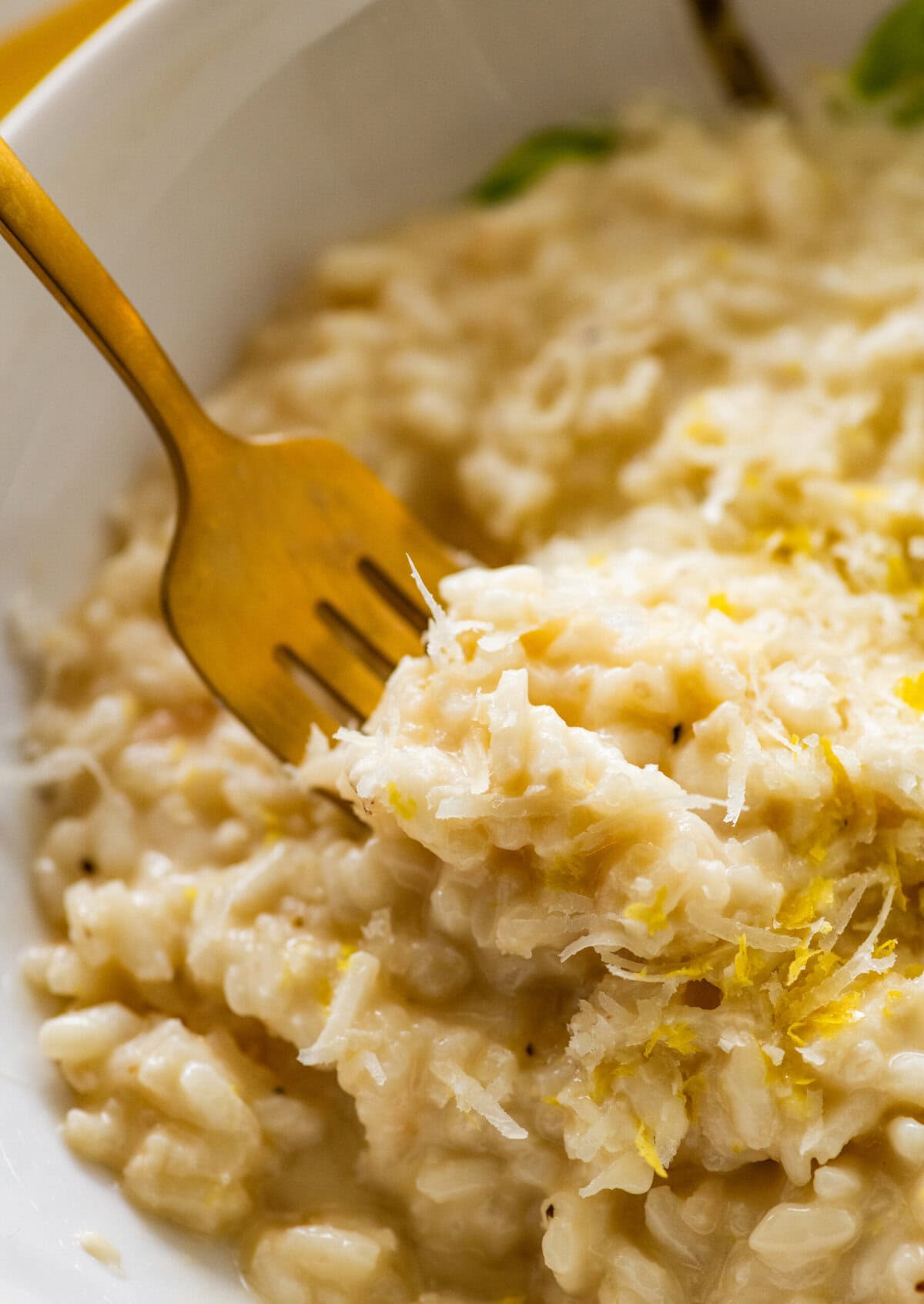 One bite of lemon risotto on a fork held over a bowl of more risotto.