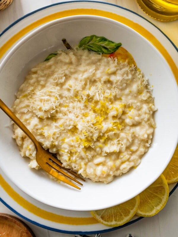 A bowl of lemon risotto with a fork resting in it and lemon slices lined on the edge of the plate.