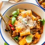 A single portion bowl of sausage and peppers pasta topped with parmesan cheese with a second bowl in the background,