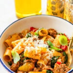 A single portion bowl of sausage and peppers pasta topped with parmesan cheese with a second bowl in the background,