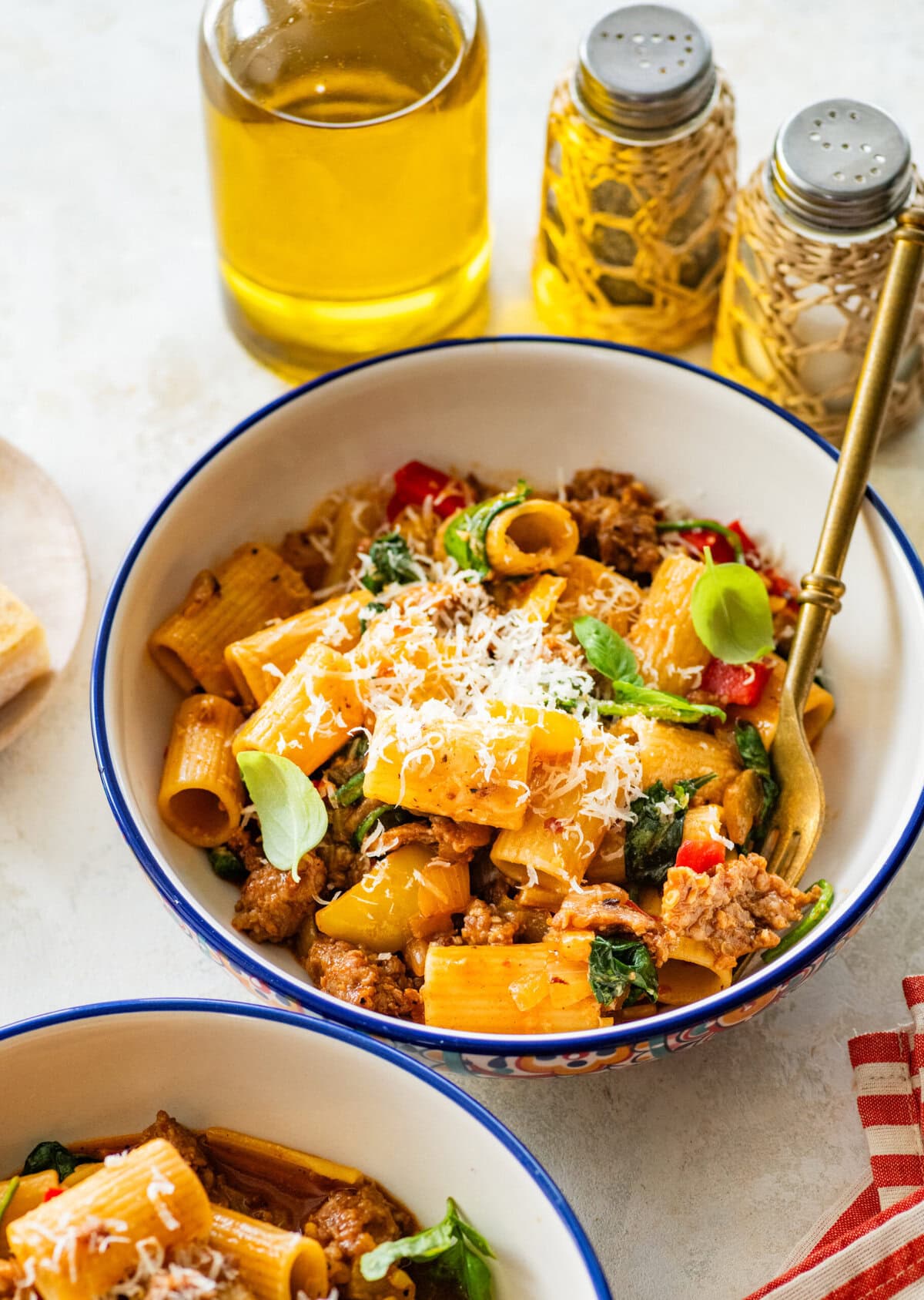 A single portion bowl of sausage and peppers pasta topped with parmesan cheese with a second bowl in the background,