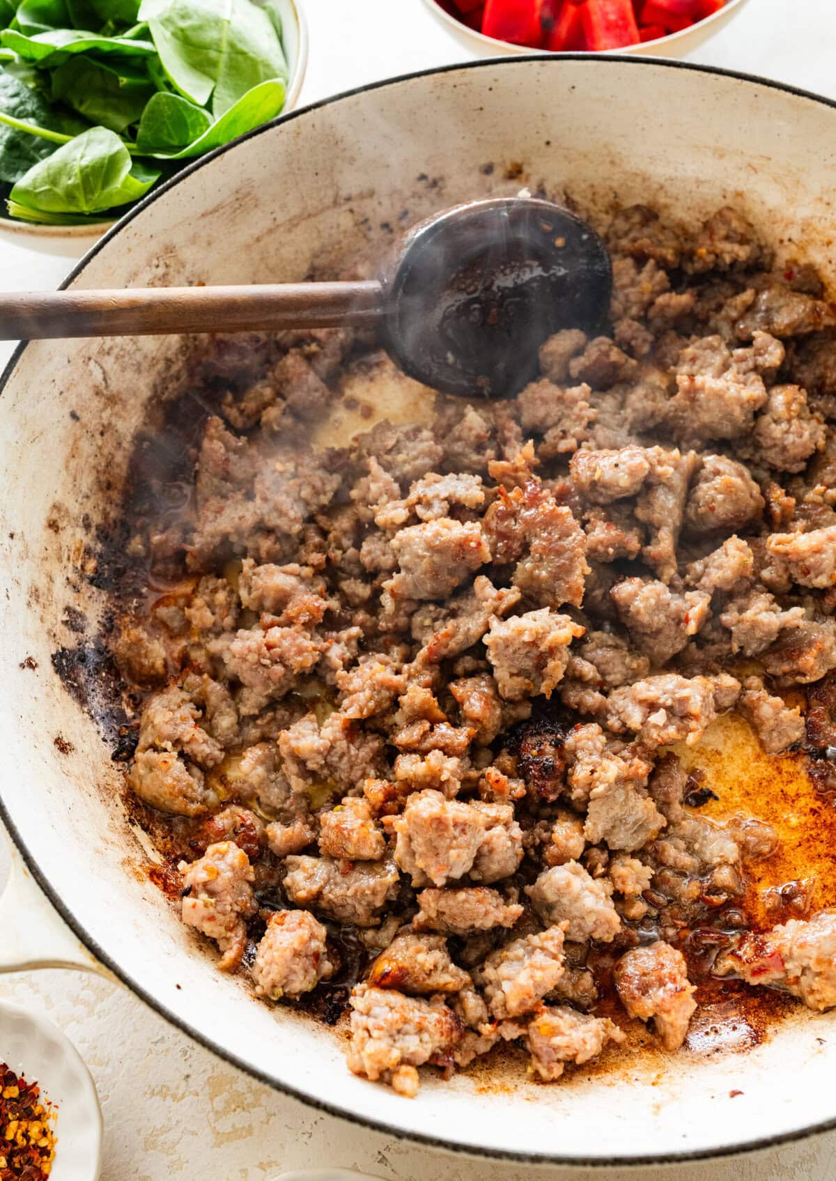 Spoon stirring cooked sausage in a pot.