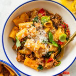 A single portion bowl of sausage and peppers pasta topped with parmesan cheese with a second bowl in the background,