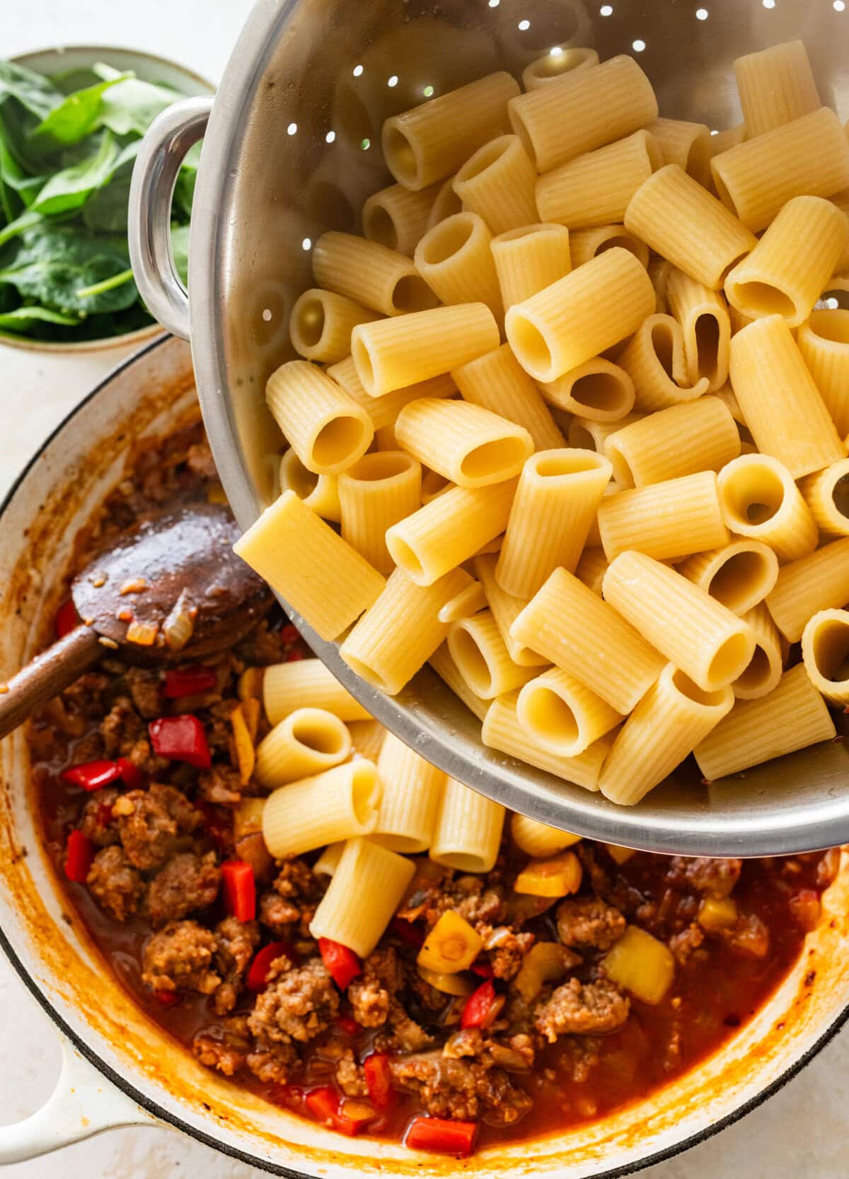 Pasta being poured from a colander to the pot of sausage and pepper mixture,