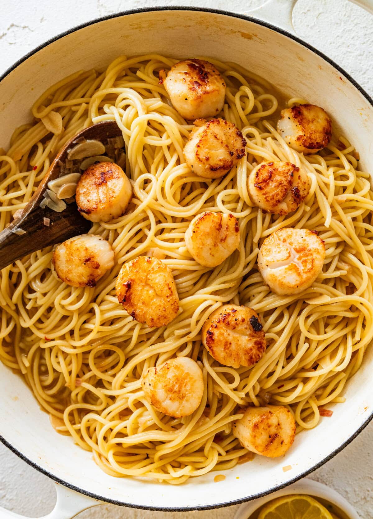 Spoon stirring together the pasta and scallops.