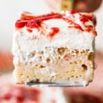 a slice of strawberry tres leches cake shown from the side, being held up by a cake server.