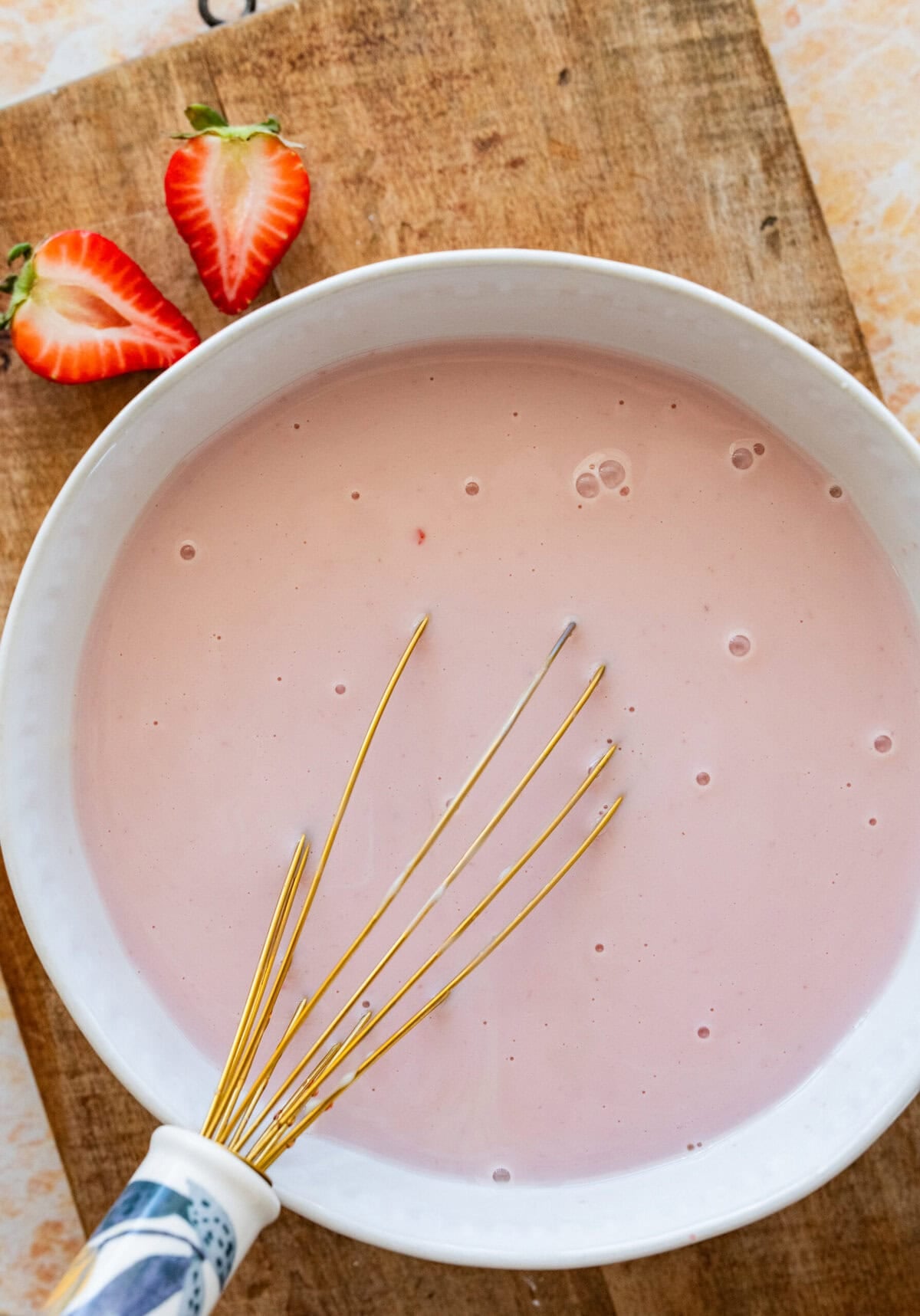 Whisk mixing the evaporated milk, condensed milk, whole milk, and strawberry syrup in a bowl.
