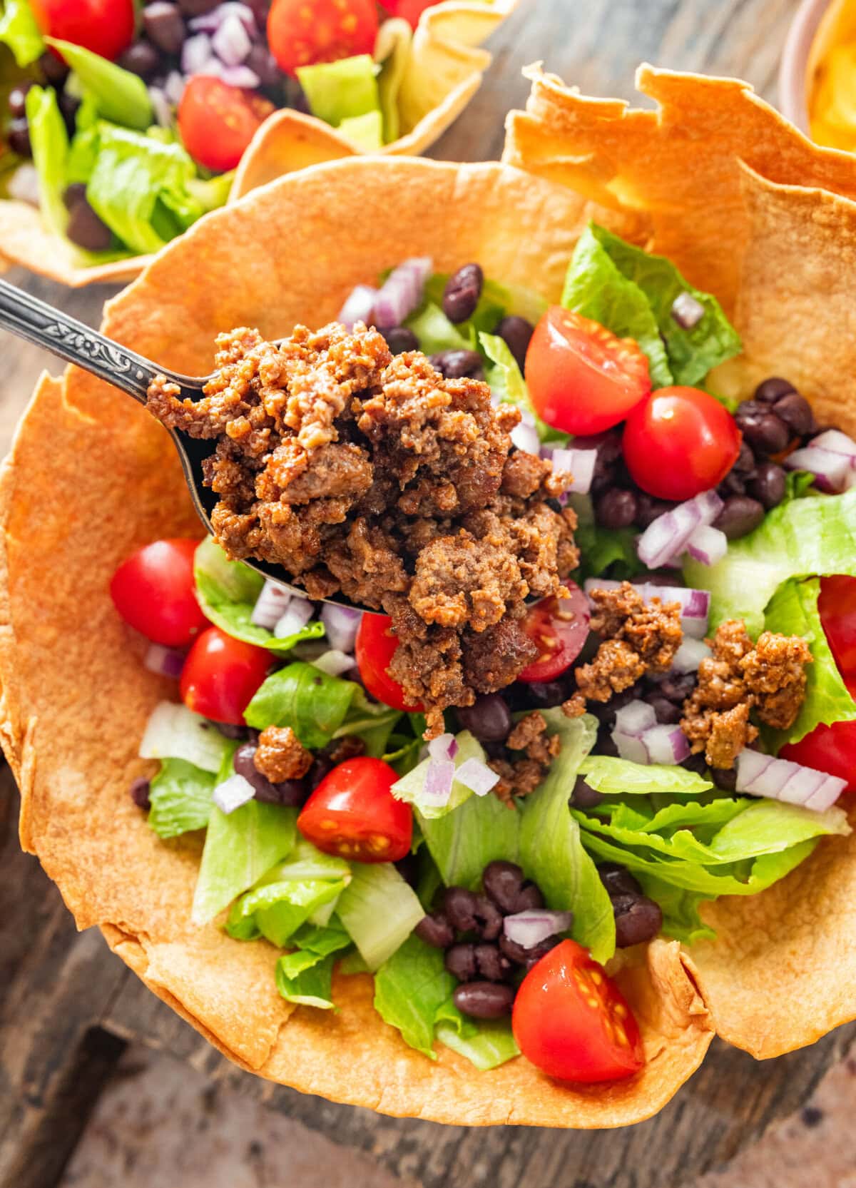 Adding beef and toppings inside a taco bowl.