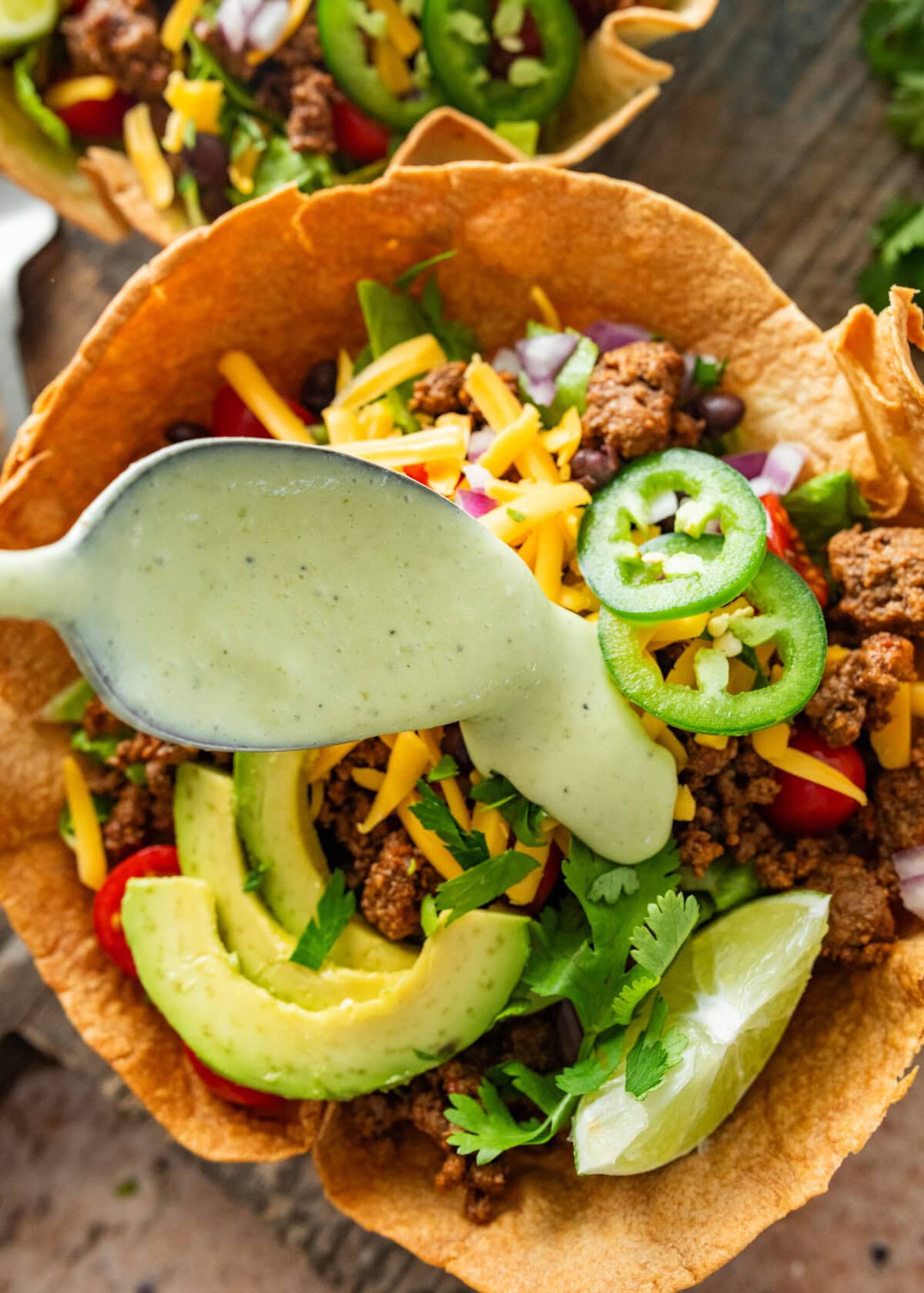 Spooning cilantro dressing over a taco bowl.