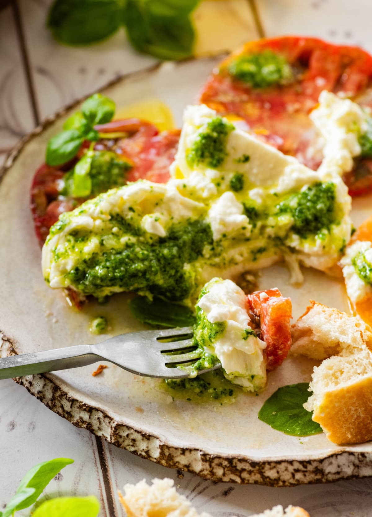 A bite of the burrata salad on a fork with a plate of more salad in the background.
