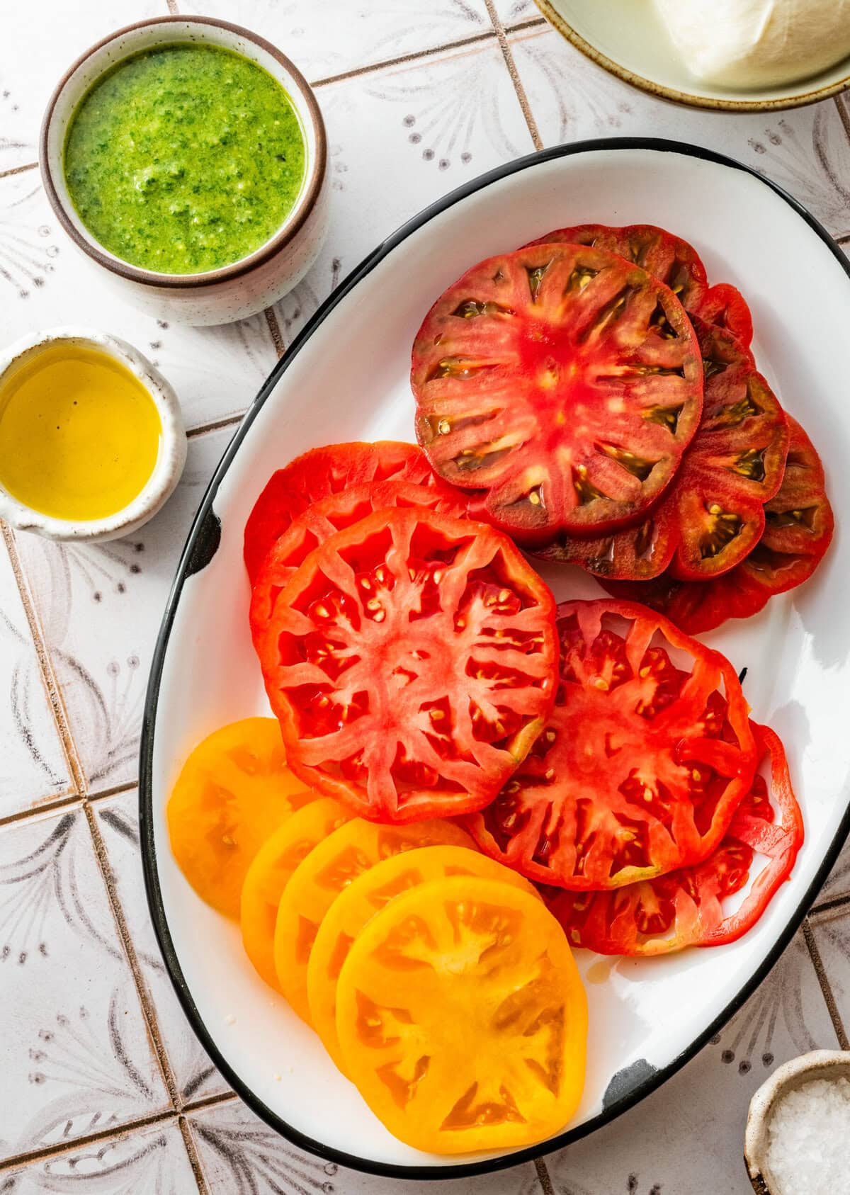 Tomato slices on a dish with the pesto and olive oil next to it.