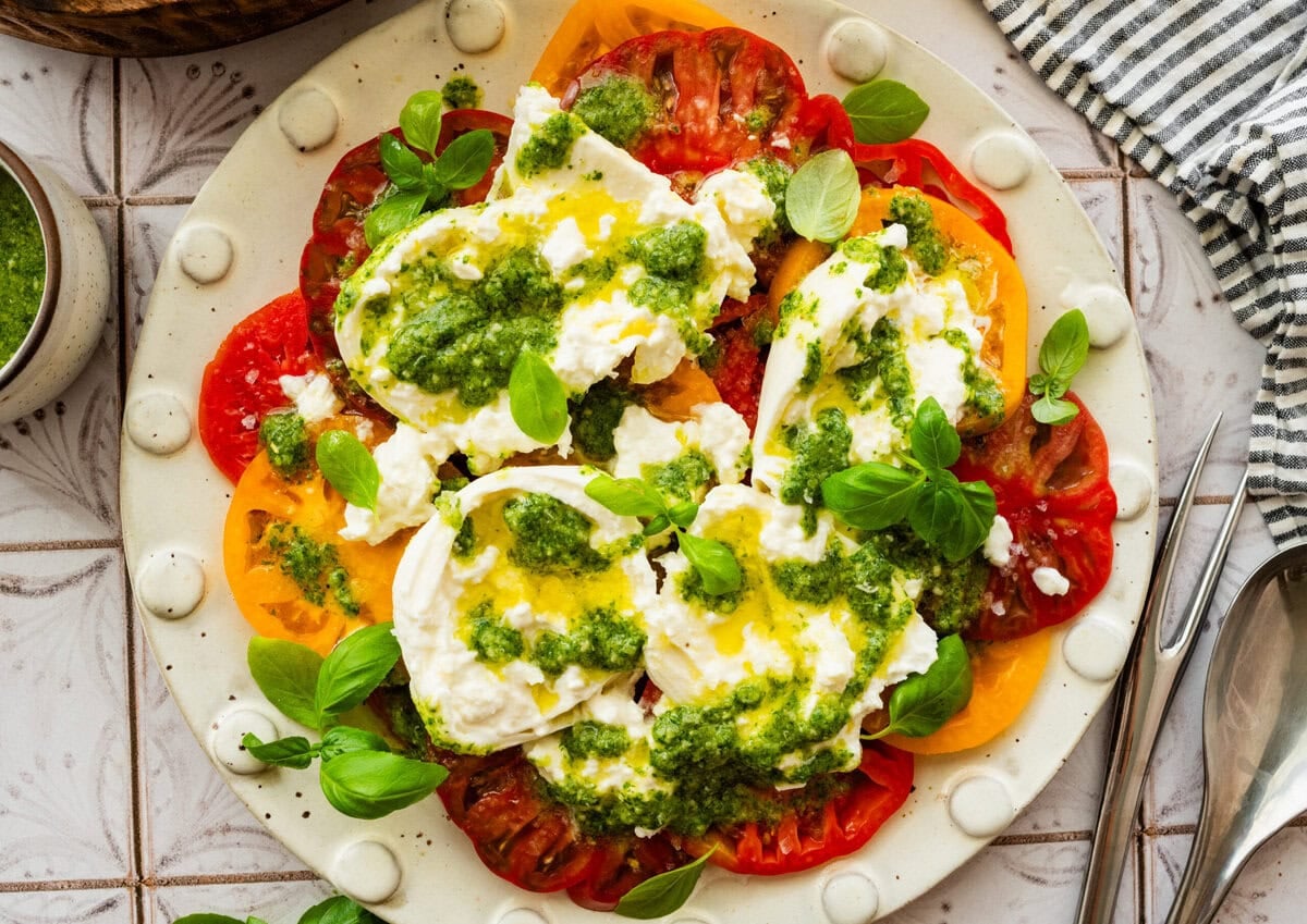 A plate of tomato burrata salad with garnish, placed next to additional ingredients.