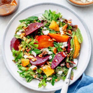 A plate of beet salad with utensils and more ingredients nearby.