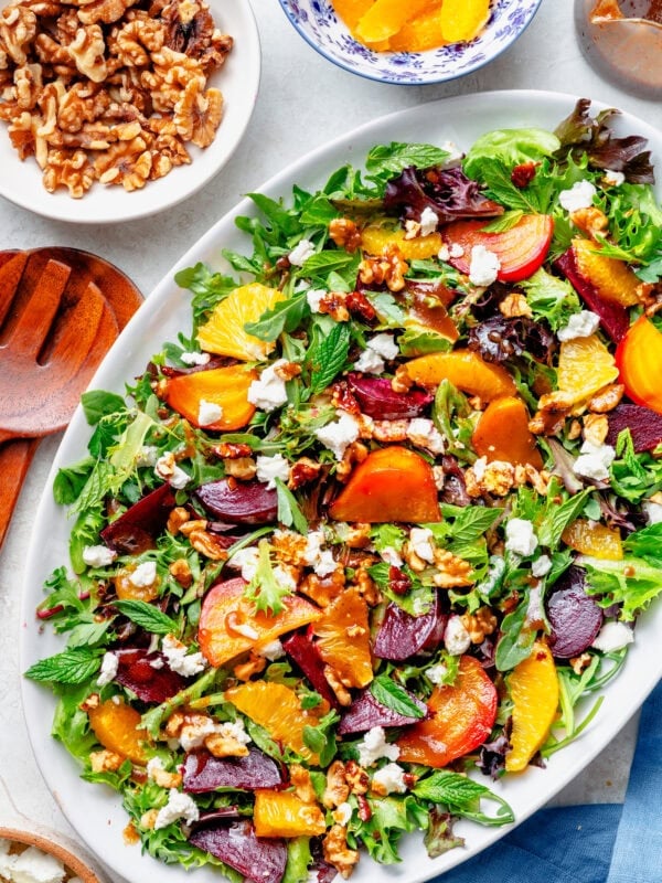 A serving plate of beet salad with more ingredients nearby.