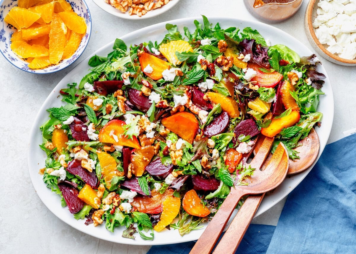 A serving plate of beet salad with utensils and more ingredients nearby.