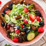 pink bowl of lettuce salad topped with goat cheese and fresh berries.