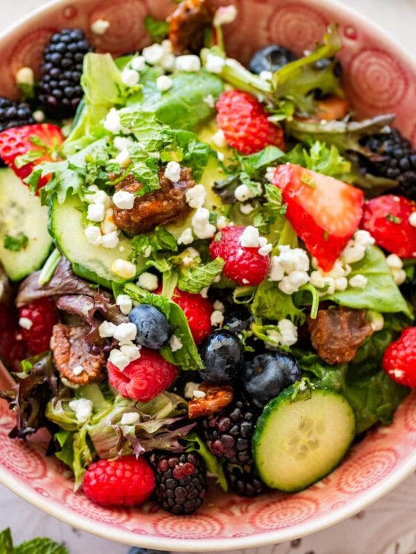 pink bowl of lettuce salad topped with goat cheese and fresh berries.