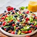 white plate of lettuce salad with fresh berries and a container of salad dressing.