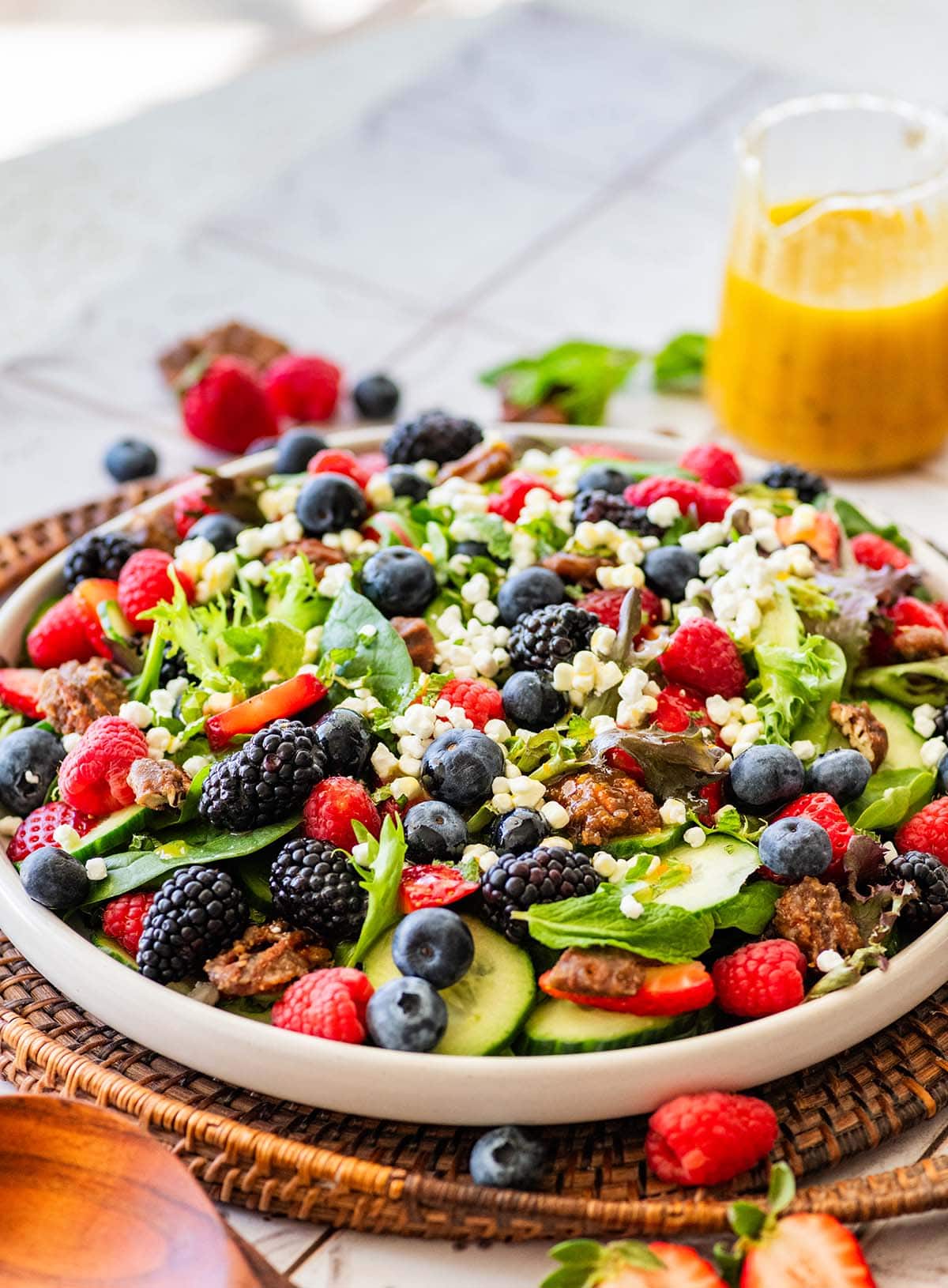 white plate of lettuce salad with fresh berries and a container of salad dressing.