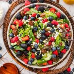 white plate of berry goat cheese salad on a wicker tray.
