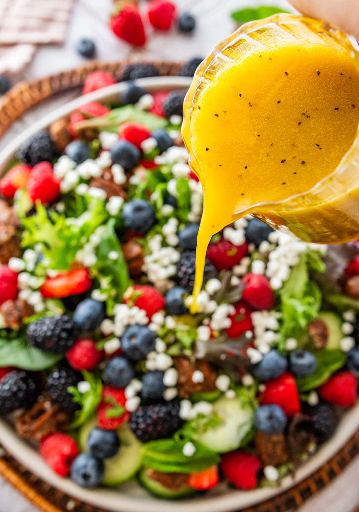 drizzling the dressing over the salad on a white plate.