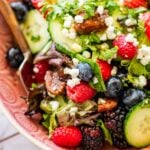 lettuce salad in a pink bowl topped with fresh berries and goat cheese.