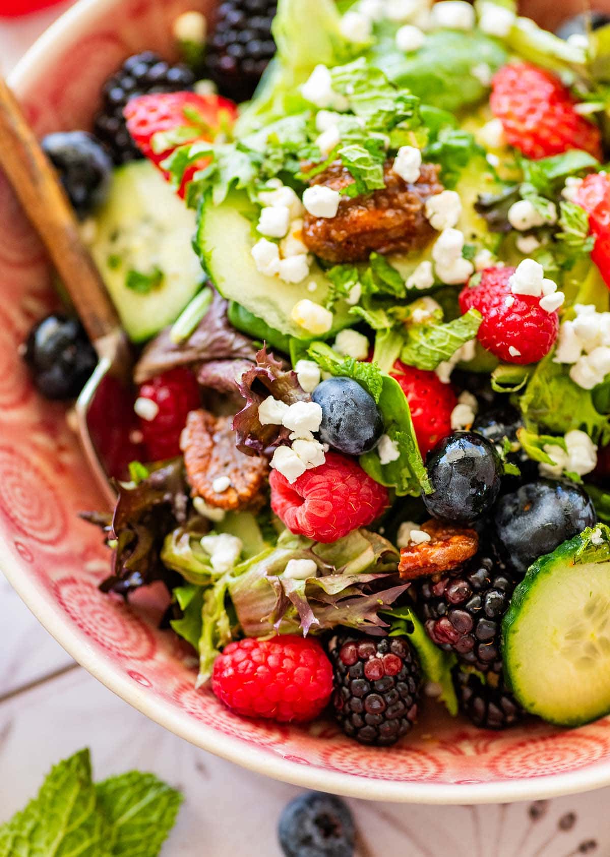 lettuce salad in a pink bowl topped with fresh berries and goat cheese.