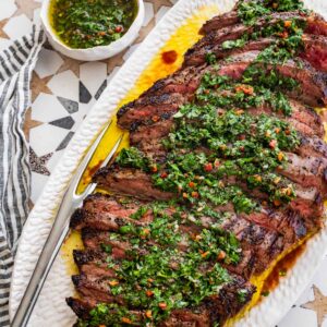 white platter of sliced grilled steak topped with chimichurri sauce.