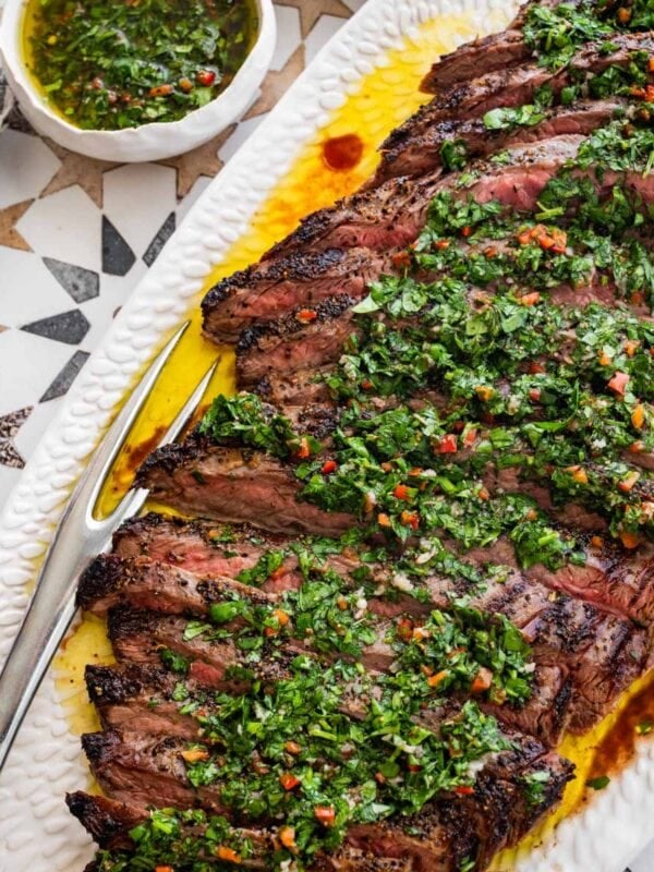 white platter of sliced grilled steak topped with chimichurri sauce.
