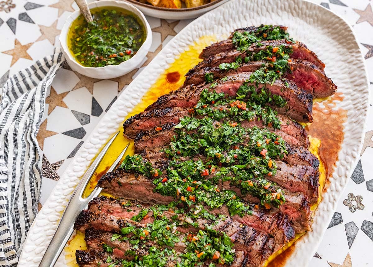 white platter of sliced grilled steak topped with chimichurri sauce.