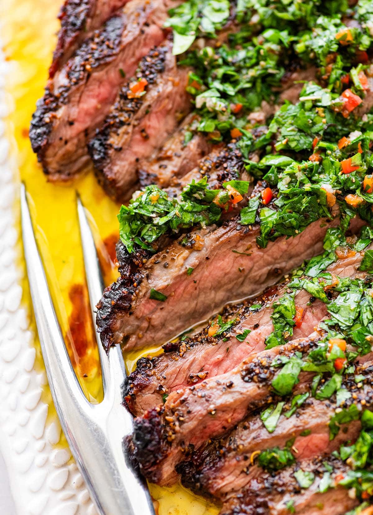 sliced steak topped with chimchurri sauce with a meat fork.