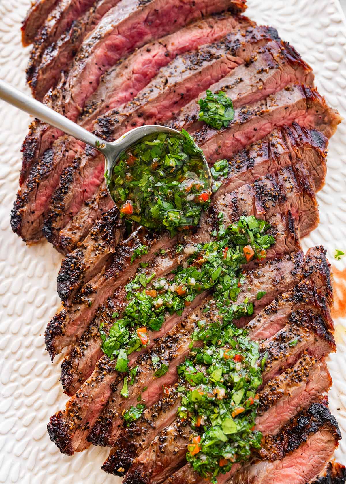 spooning the chimichurri sauce over the sliced grilled steak.