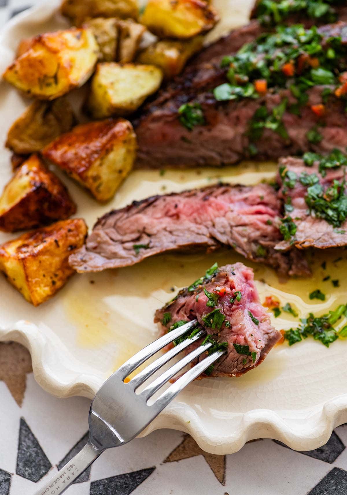 holding a forkful of grilled flank steak with chimichurri.