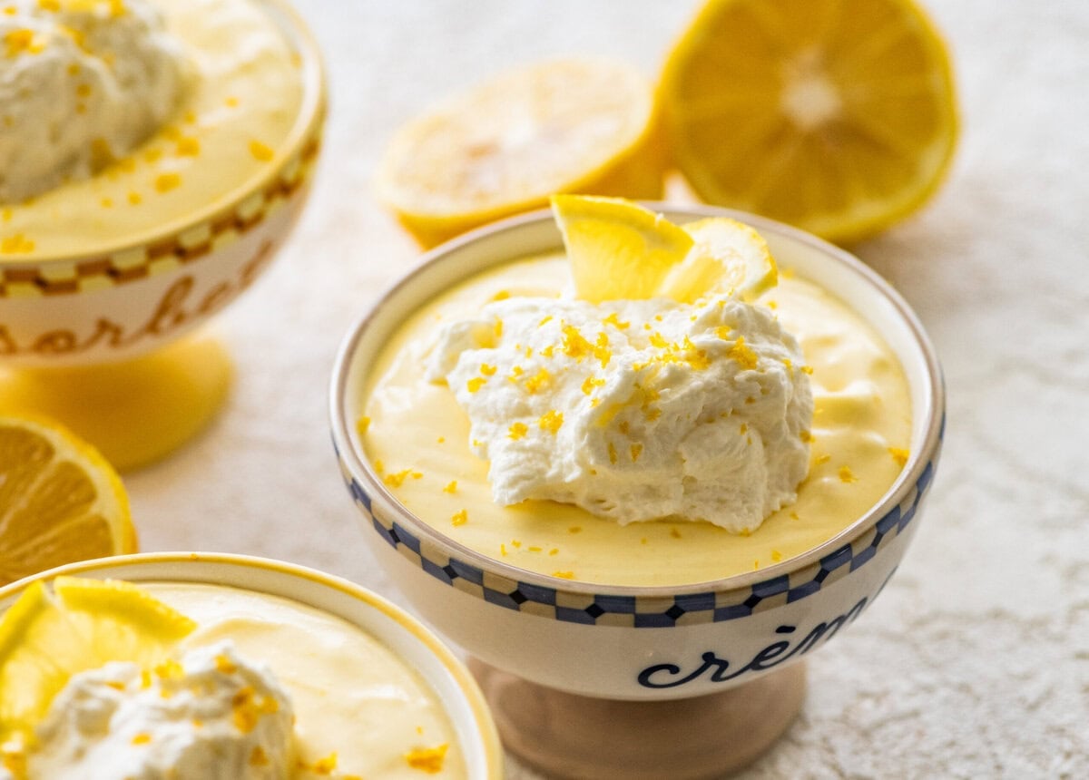 One serving of lemon mousse in a bowl with garnish and more ingredients in the background.