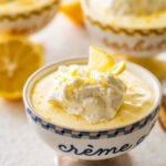 One serving of lemon mousse in a bowl with garnish and more ingredients in the background.