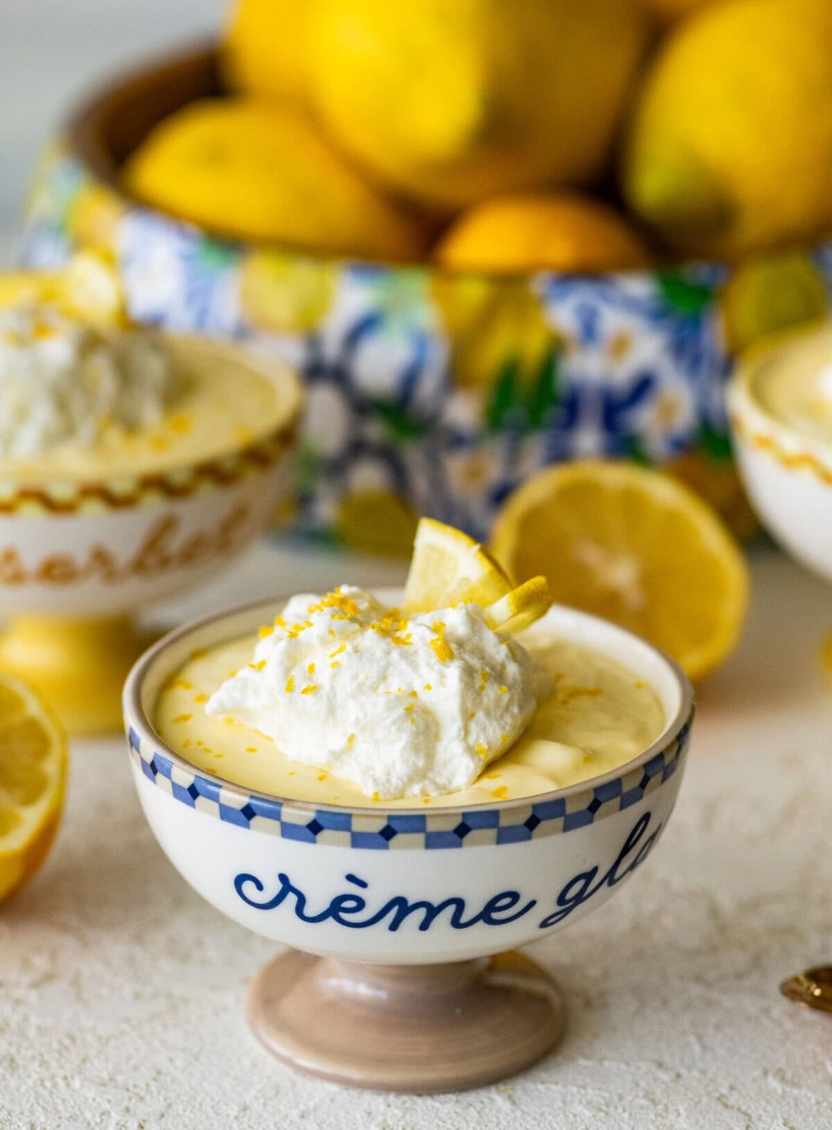 One serving of lemon mousse in a bowl with garnish and more ingredients in the background.