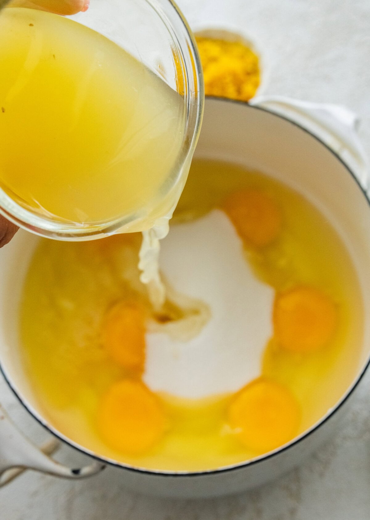 A bowl of unmixed eggs, salt, and lemon zest, with lemon juice being poured in.