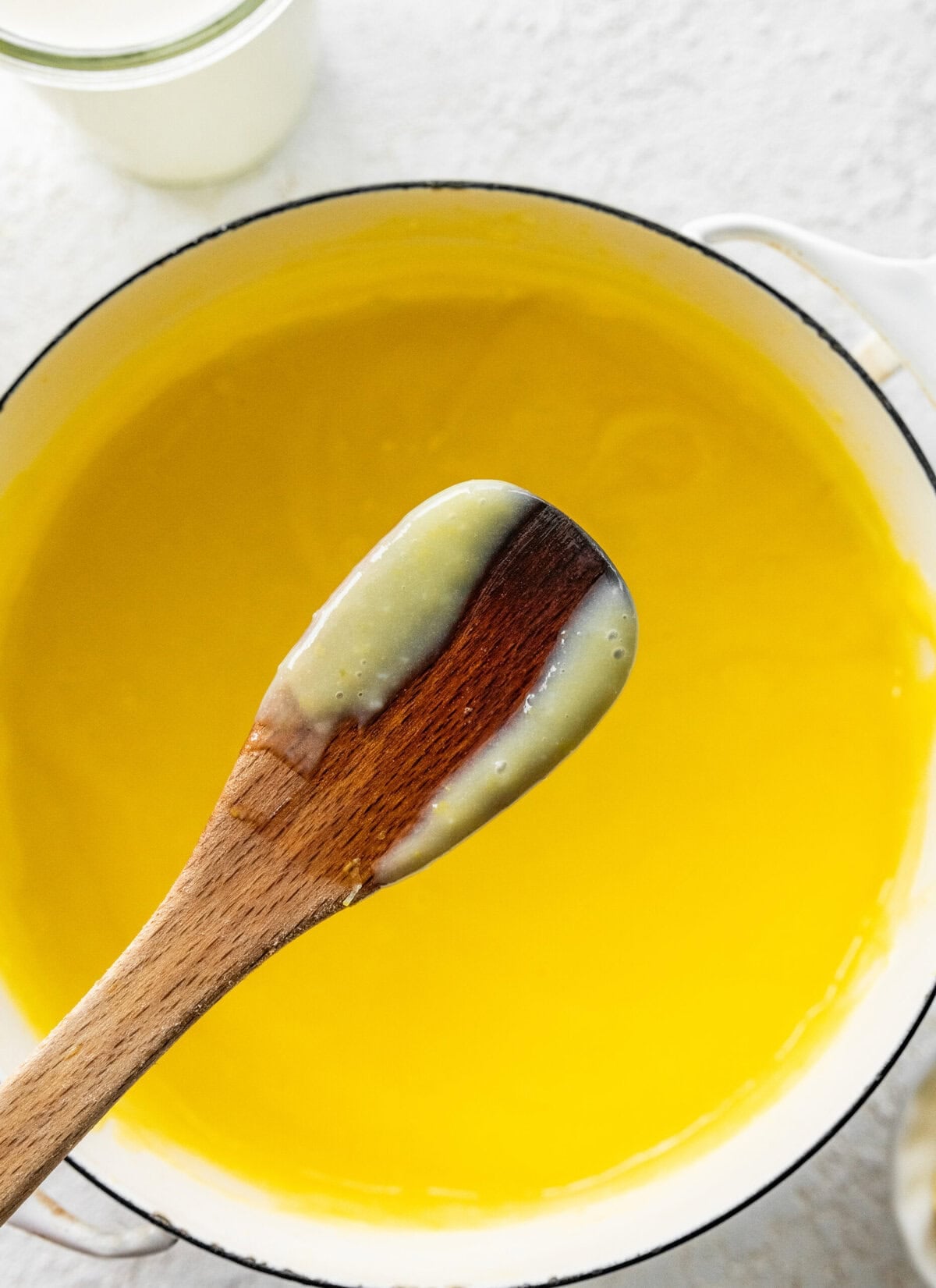 Lemon curd in a pot after cooking on stove, with a wooden spoon showing some.